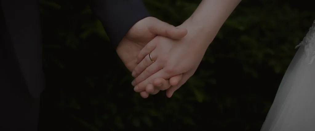 Close-up of a couple holding hands, a physical touch; a wedding ring shows on one finger.