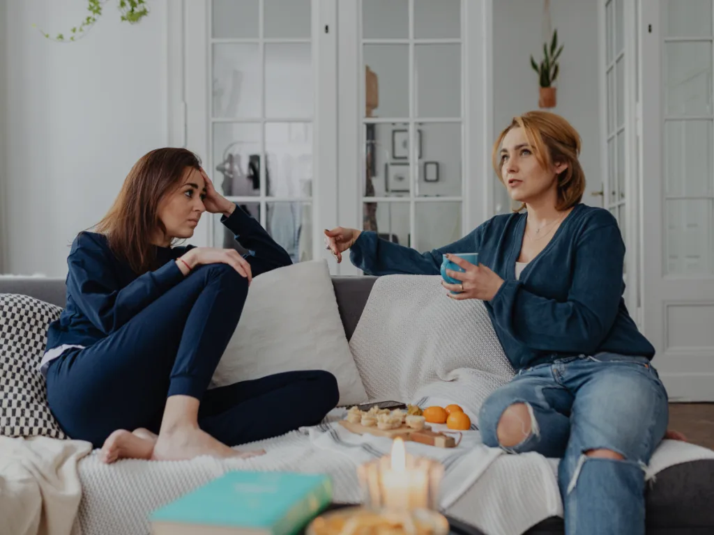 Two women talking while sitting in a couch.